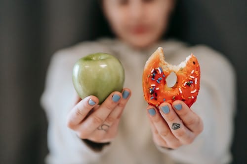 Free Woman showing apple and bitten doughnut Stock Photo