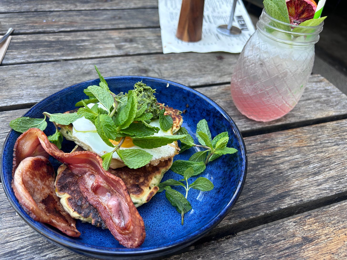 A plate of hotcakes with bacon, egg, pesto and mint, plus an almost empty glass of iced tea.