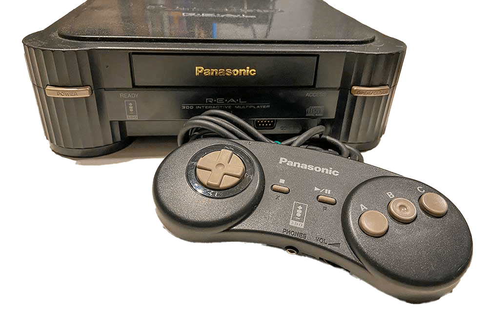 A photo of the Panasonic 3DO situated behind its standard controller. There is a D-pad on the left, and three face buttons on the right, with additional buttons (X and P) where you expect Select and Start buttons to be.