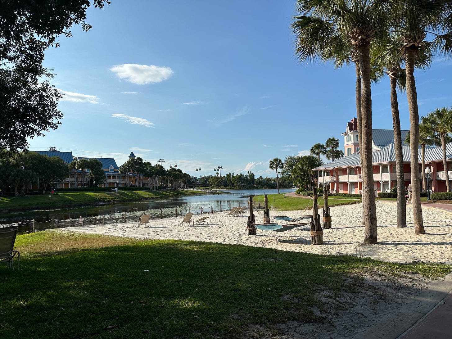 View of two sections of Caribbean Beach Resort, separated by water, with a white sand beach and palm trees in the foreground