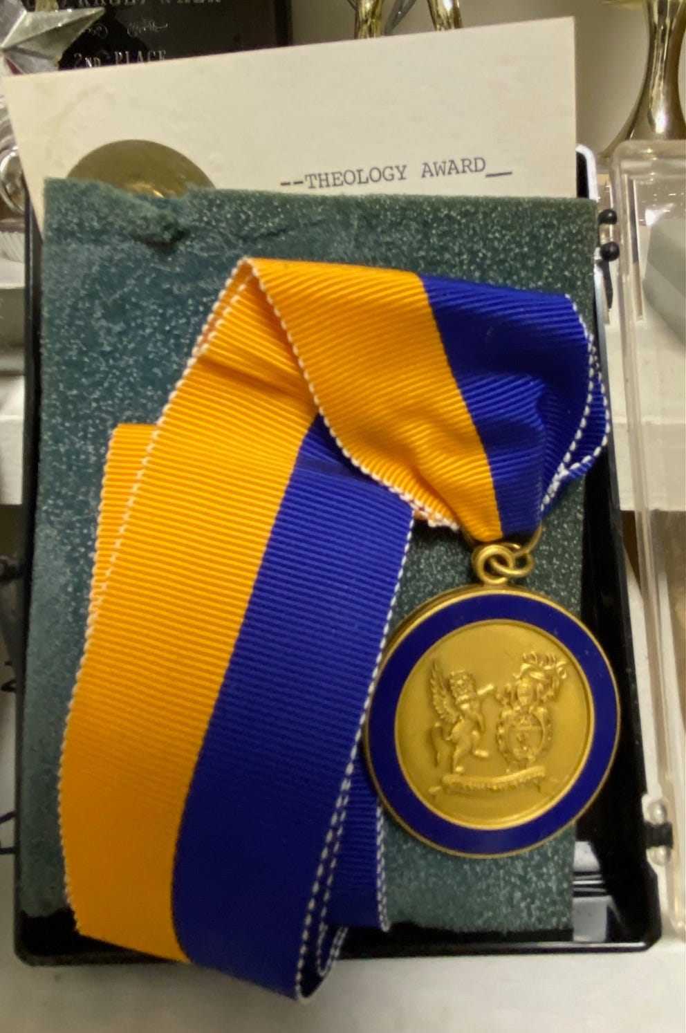 Photo of a gold and blue medal on a long, folded over gold and blue ribbon. A small card in the box reads: Theology Award.