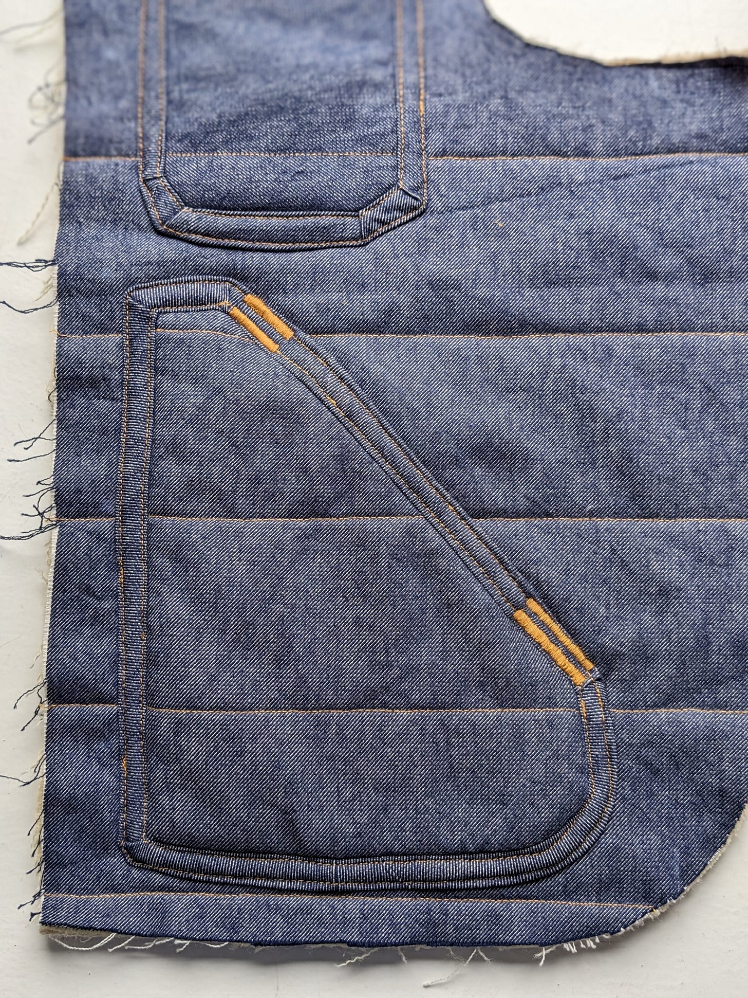 An in progress photo of the front of a quilted denim vest, showing the front and chest pockets