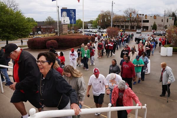 Two lines of fans leading up a set of stairs, snaking back toward an intersection outside Bon Secours Wellness Arena.