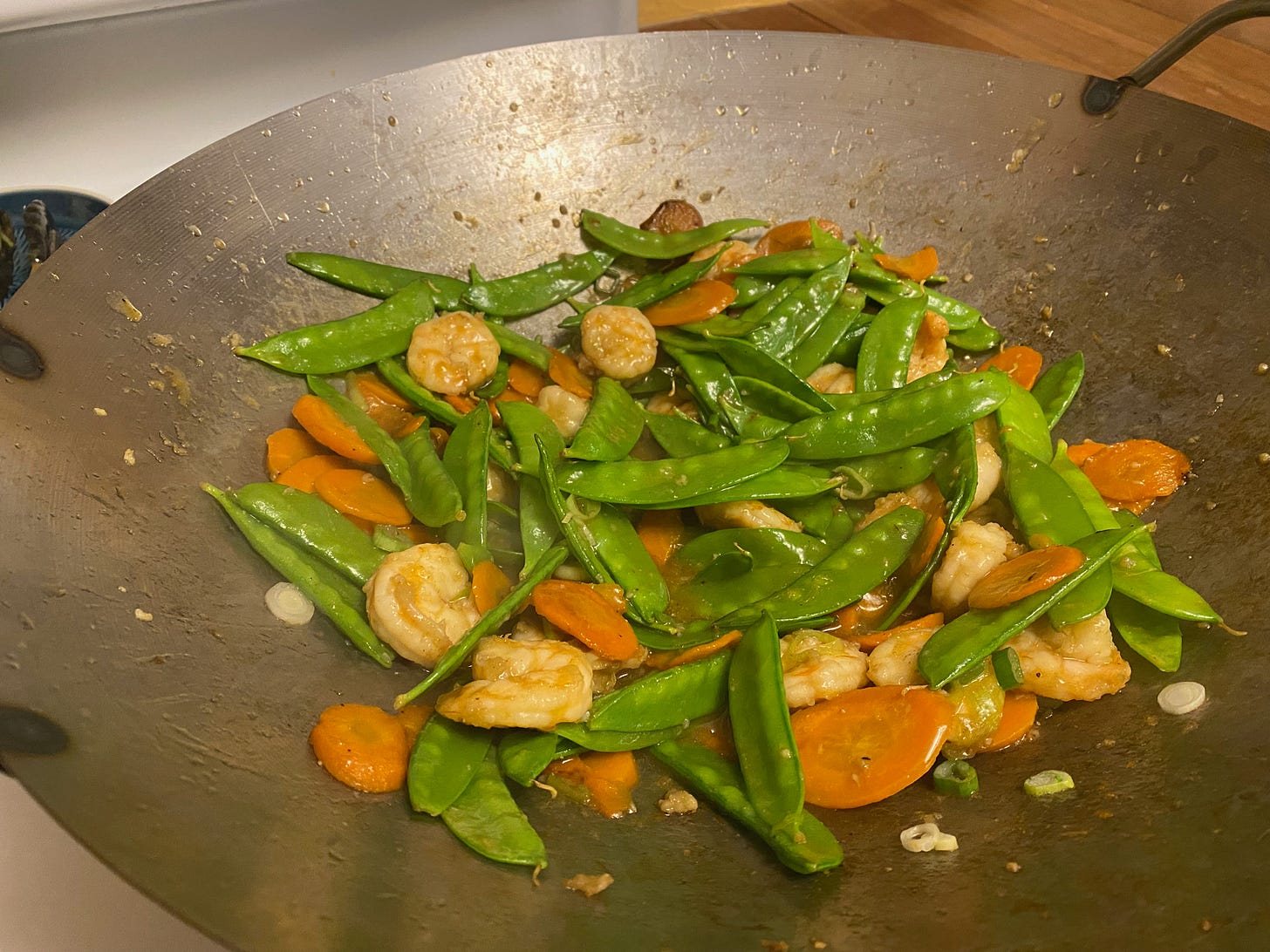 A wok full of stir-fried shrimp, snow peas, and carrots.