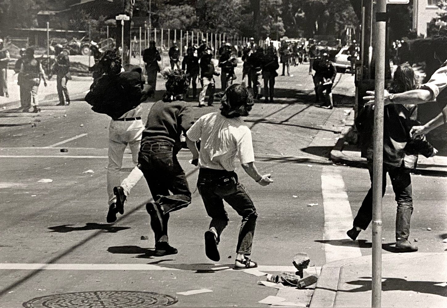 Three protestors on the street level throw objects at an advancing line of police.