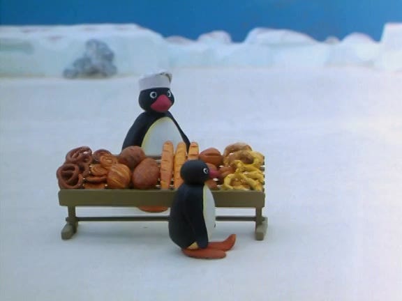 screencap of penguin from Pingu selling a cart of baked goods to another penguin