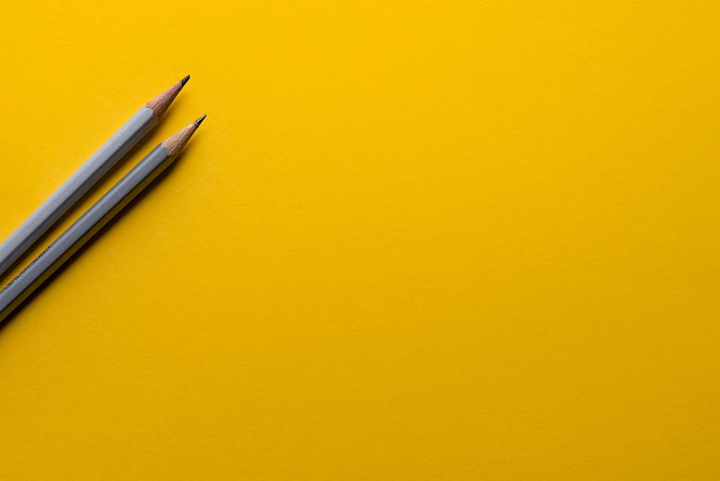 Two pencils on a blank yellow background