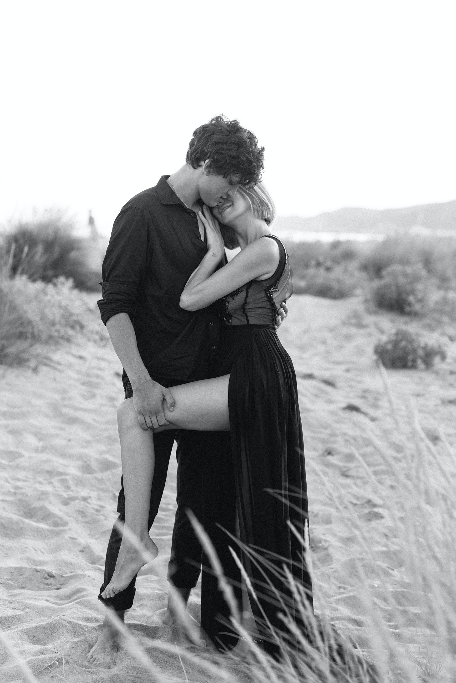 Man woman outside in sand dune with woman wearing dress, black and white