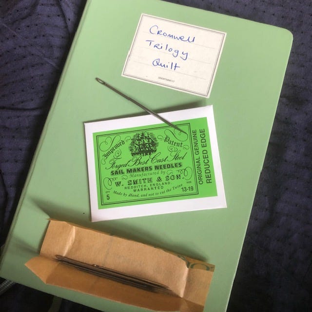 An open packet of large long and thick sailmakers' needles, on top of a notebook with the label "Cromwell Trilogy Quilt"