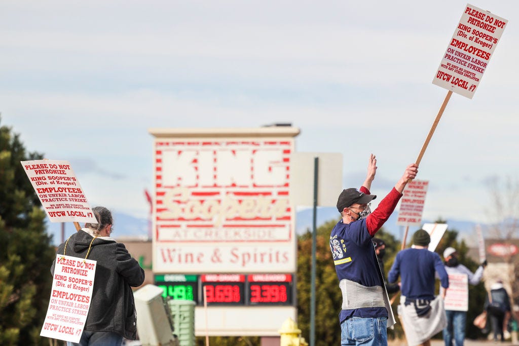 protestors walking and carrying signs in front of a king soopers store signe