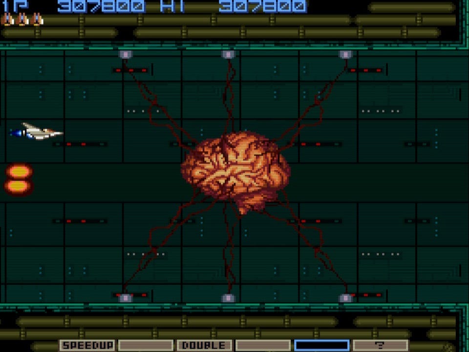 A screenshot from the beginning of the encounter against the final boss of Gradius, a giant brain that you destroy without it resisting at all. It's hooked up to a number of outlets on the ceiling and floor, but those will all detach as you destroy the brain.