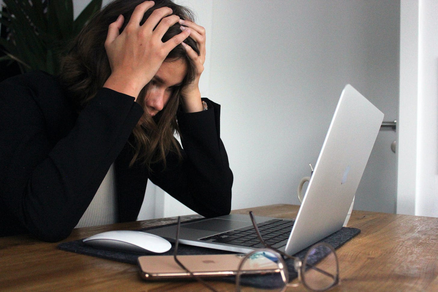 Woman looking at a laptop with her hands on her head indicating that she is stressed or is at a loss
