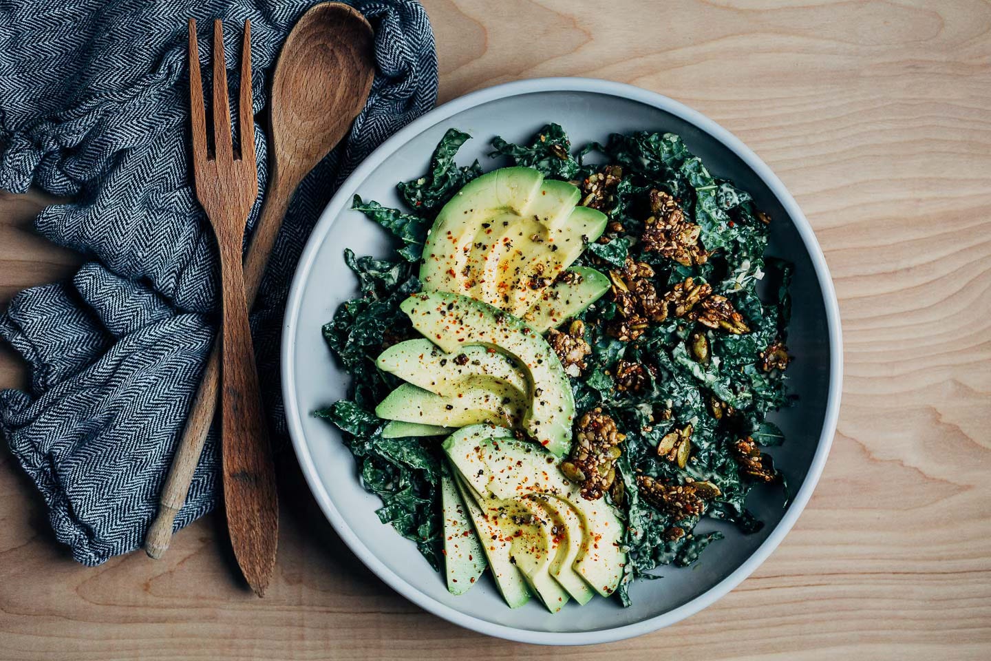 A bowl of kale and avocado salad with serving utensils and a napkin alongside