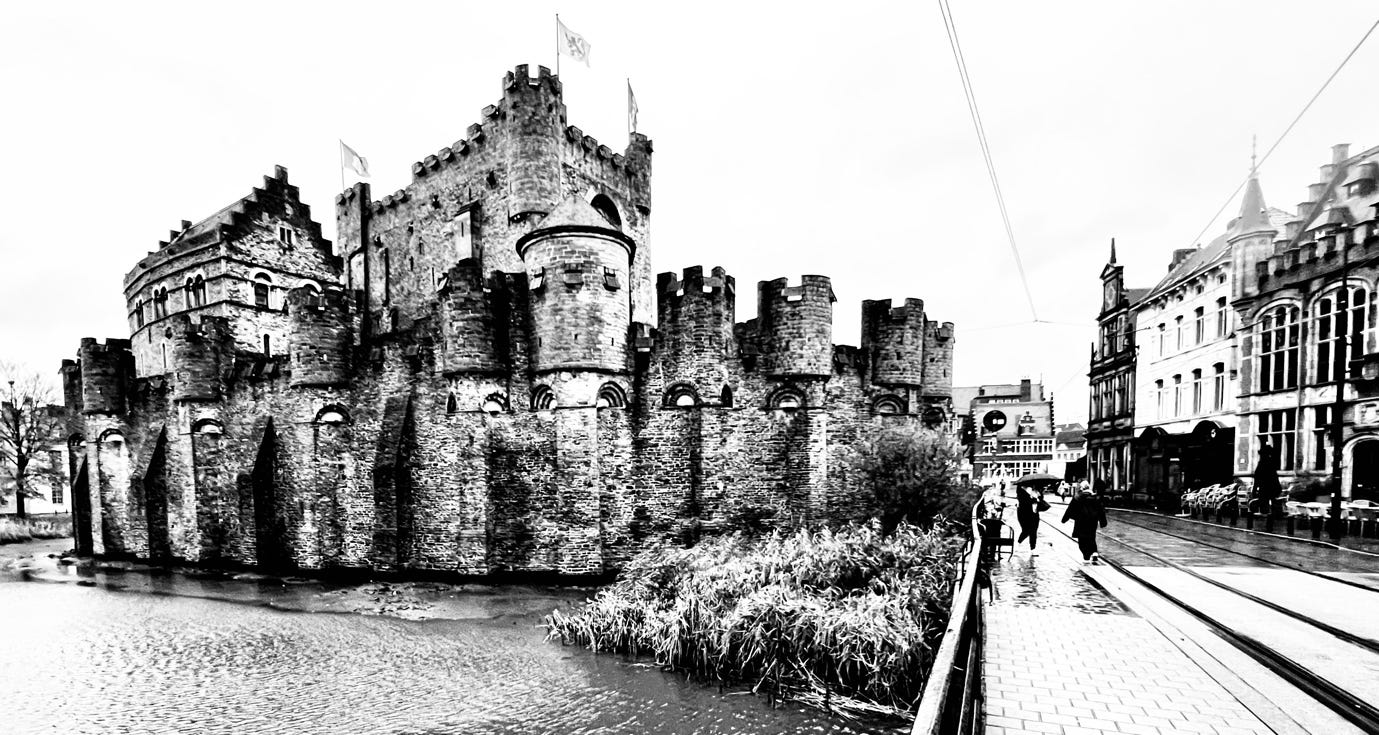 A stone castle with a bridge and people walking

Description automatically generated