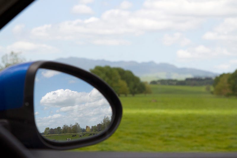 Looking out a car window and the side mirror, with country scenes reflected in it.