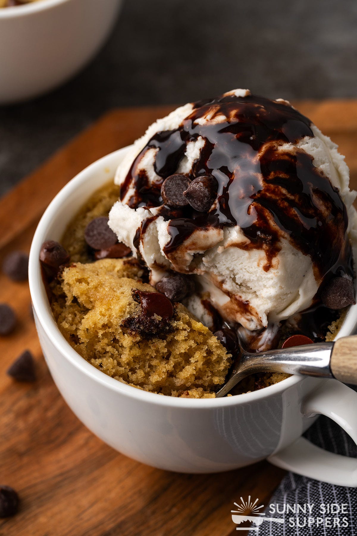 A chocolate chip cookie in a mug with ice cream and chocolate syrup.