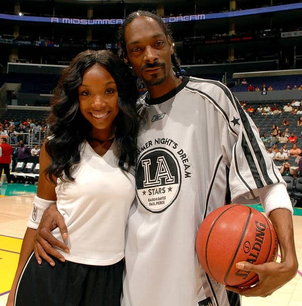Two people on a basketball court pose for a photo. One holds a basketball, wearing a sports jersey, the other wears a sleeveless top