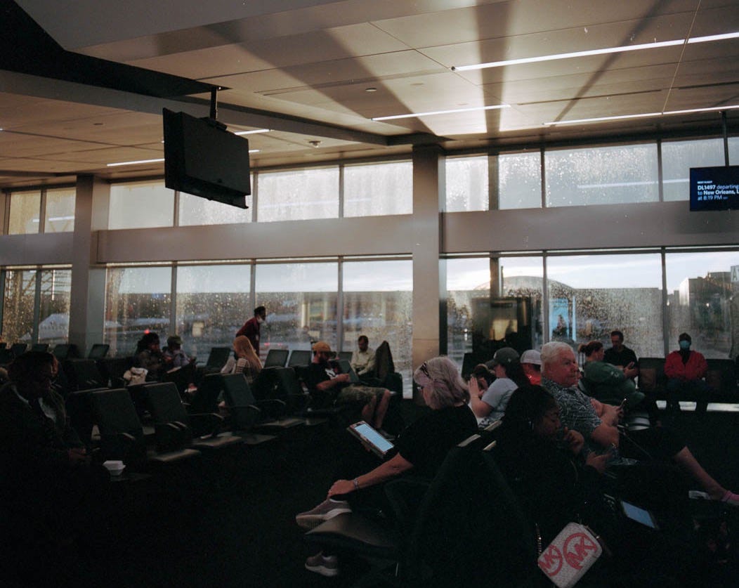 A photograph of people waiting at an airport gate with light streaming through the windows and rain on the windows.