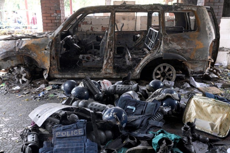 Damaged riot gear of security forces is seen next to a burnt vehicle outside a police station, in Dhaka