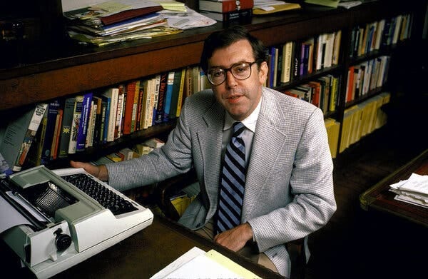 Kevin Phillips, a dark-haired man wearing a checked sports jacket, a striped tie and glasses, sits at a typewriter in front of a bookcase.