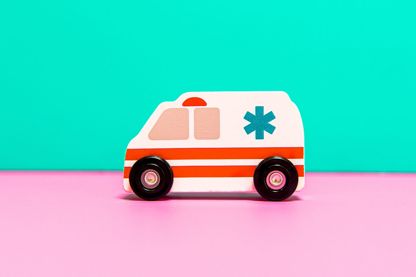a toy ambulance on a pink table with a turquoise background