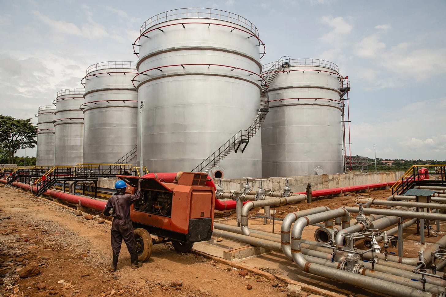 A worker adjusts a generator in front of fuel storage tanks at an oil logistics complex in Entebbe, Uganda.