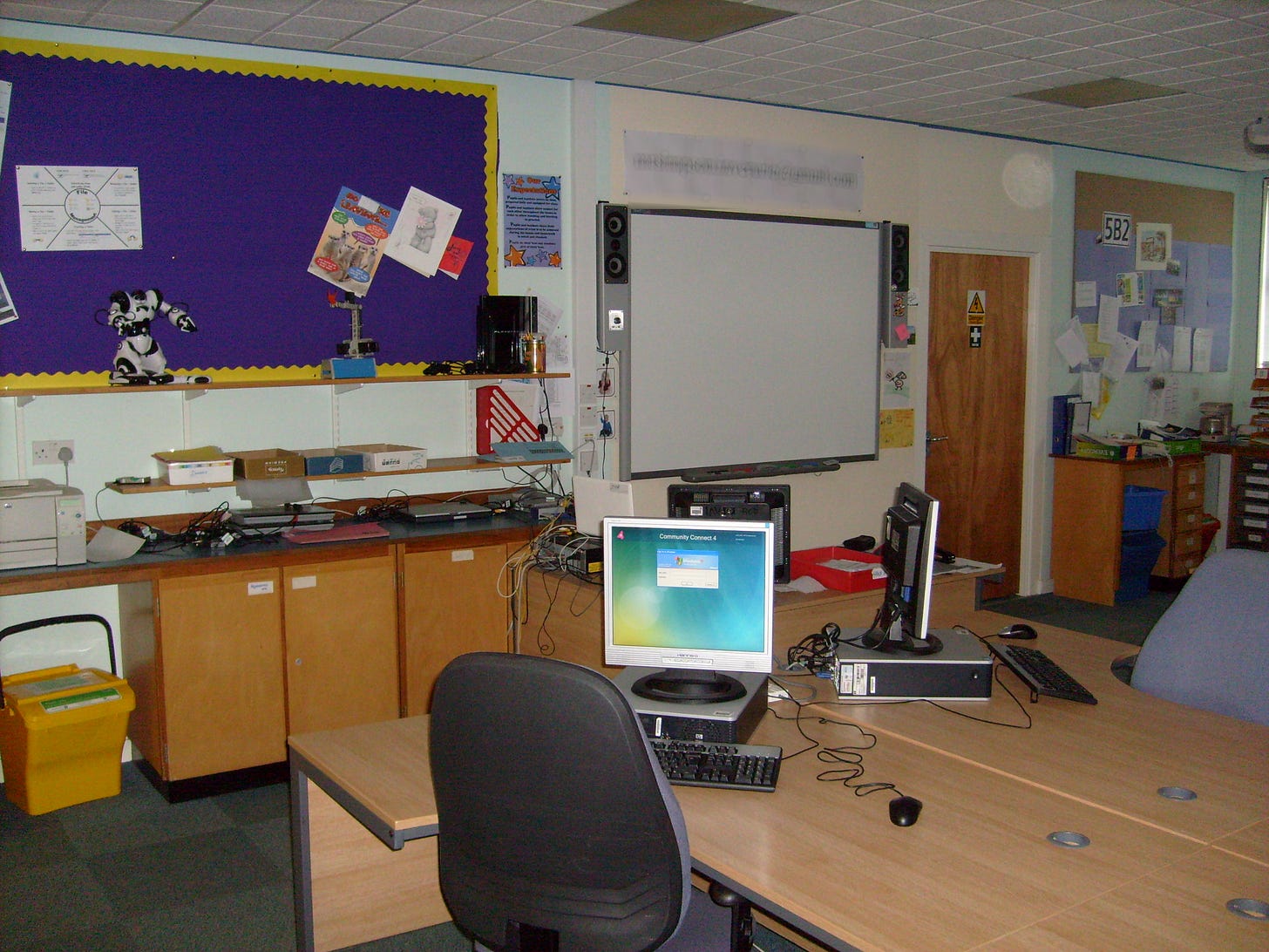 A Computing Science classroom with office desks, a robosapien on a shelf, a smartboard and a coffee machine in the far corner