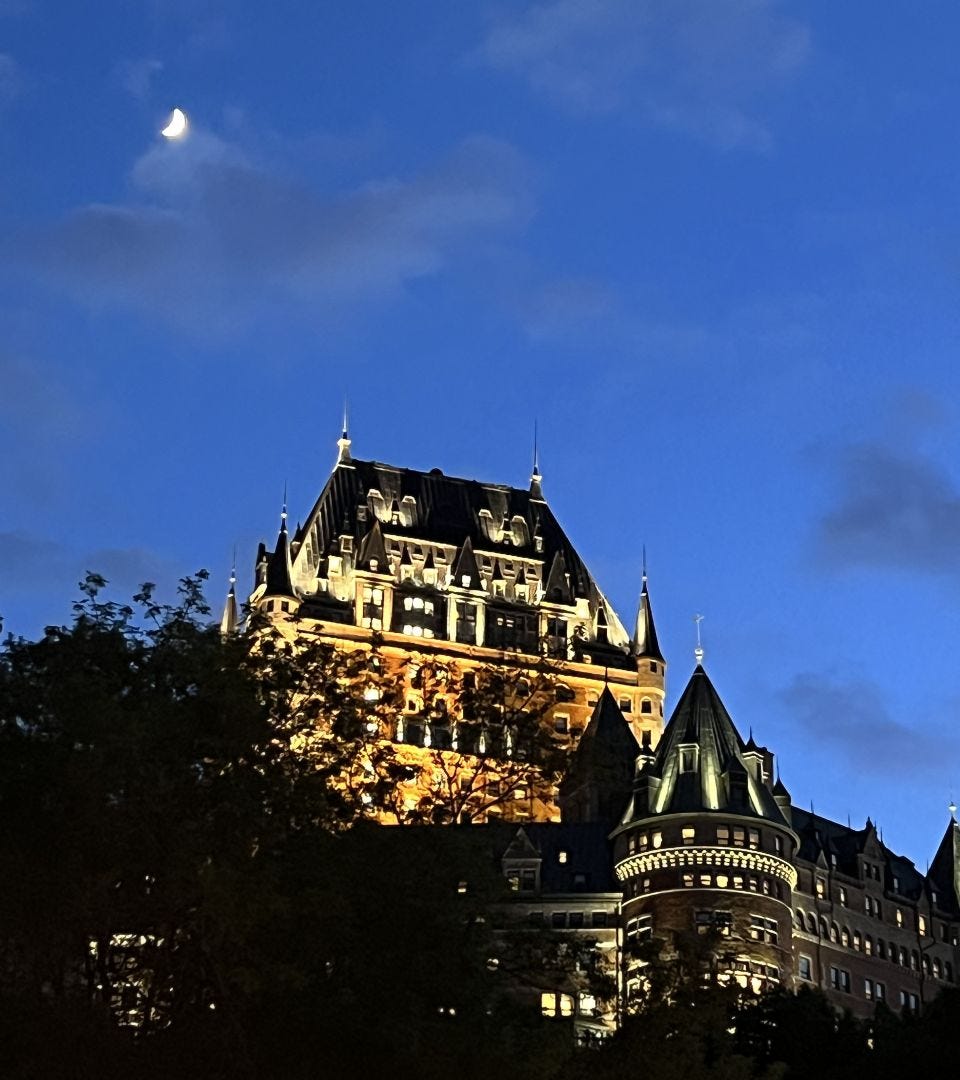 Quebec City's Chateau Frontenac hotel with a crescent moon hanging over it in the evening sky.