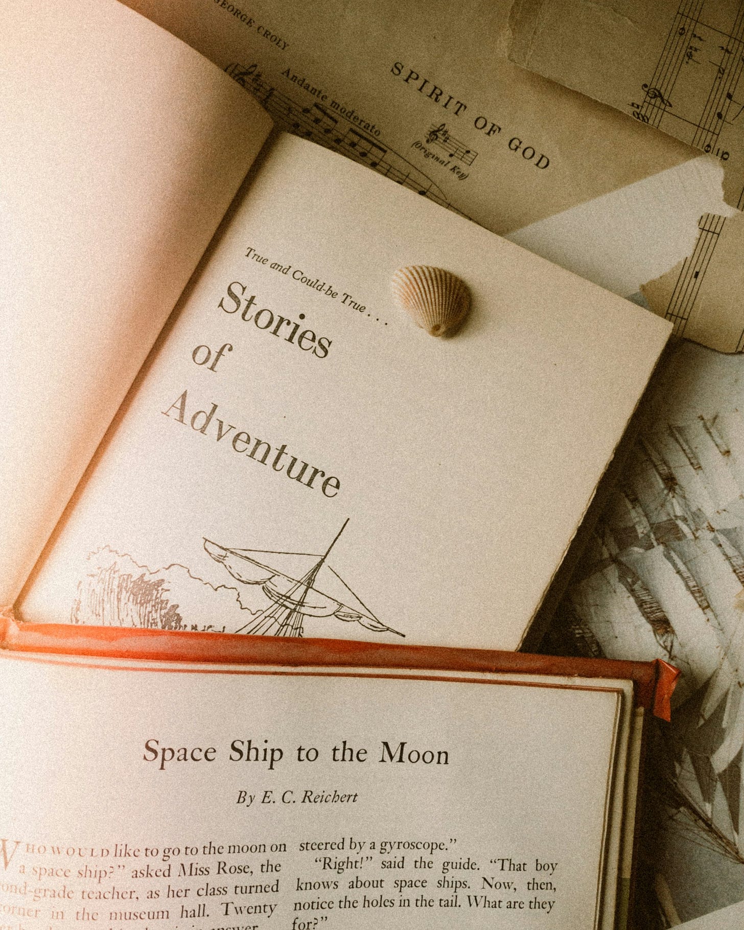 Open books titled “Stories of Adventure” and “Space Ship to the Moon” lay on top of a music score titled “Spirit of God” 
