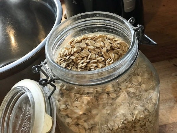 An open glass jar of oats with metal bowl in background