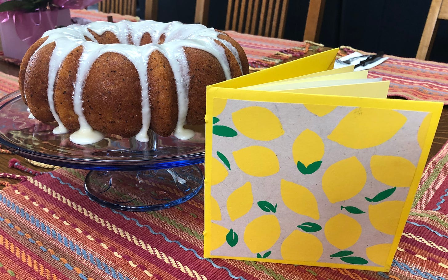 A lemon Bundt cake with a card in front of it. The card has images of lemons on the face.