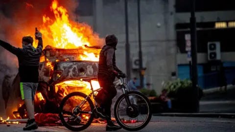 Getty Images Rioters and a car on fire