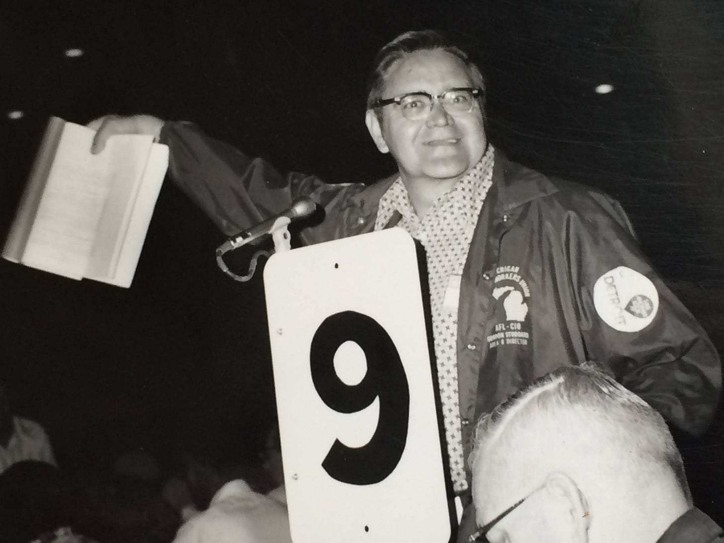 a black and white photo of my grandpa, probably from the 1960s or 1970s. He's wearing an AFL-CIO jacket and looking at the camera with a smile. He's a white man wearing black-rimmed glasses.