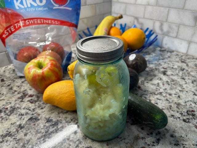 A mason jar with homemade sauerkraut and several different kinds of fruits and vegetables.