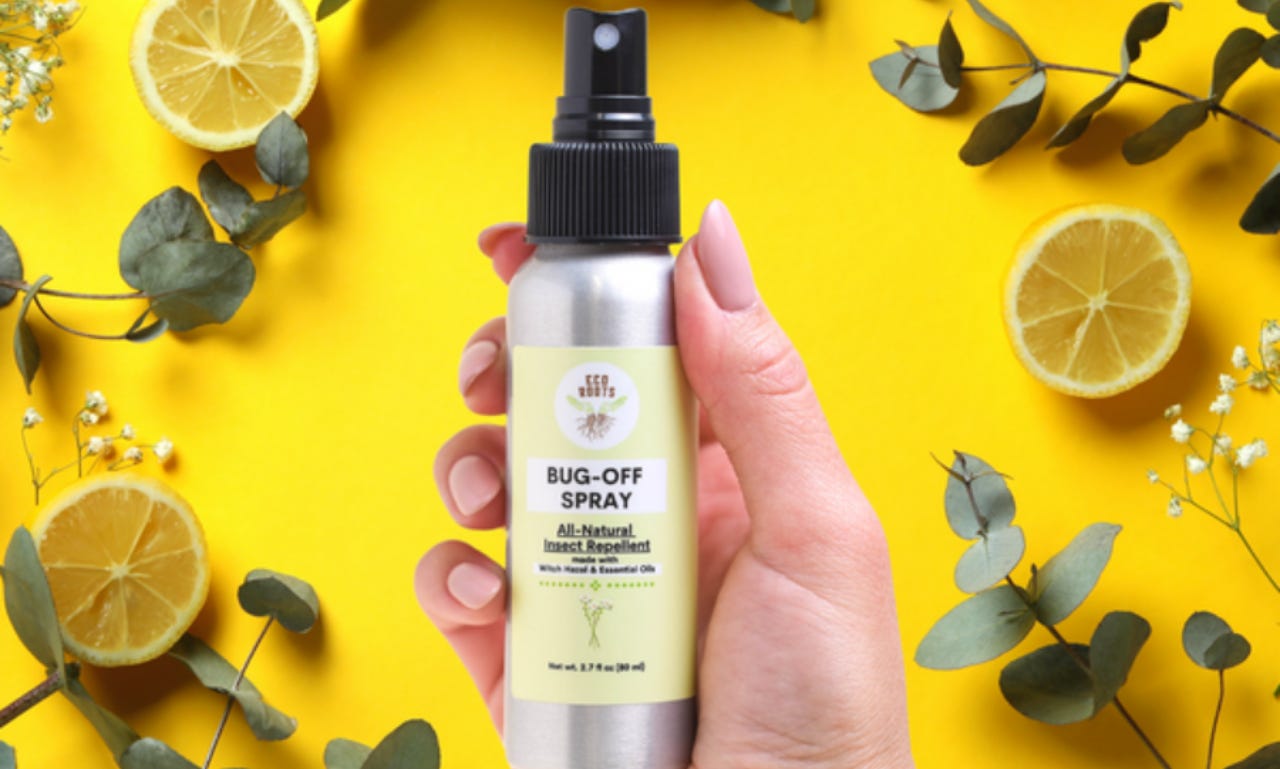 a hand holds a spray bottle of ecoroots's natural bug spray. the background is yellow, with lemons, baby's breath, and eucalyptus