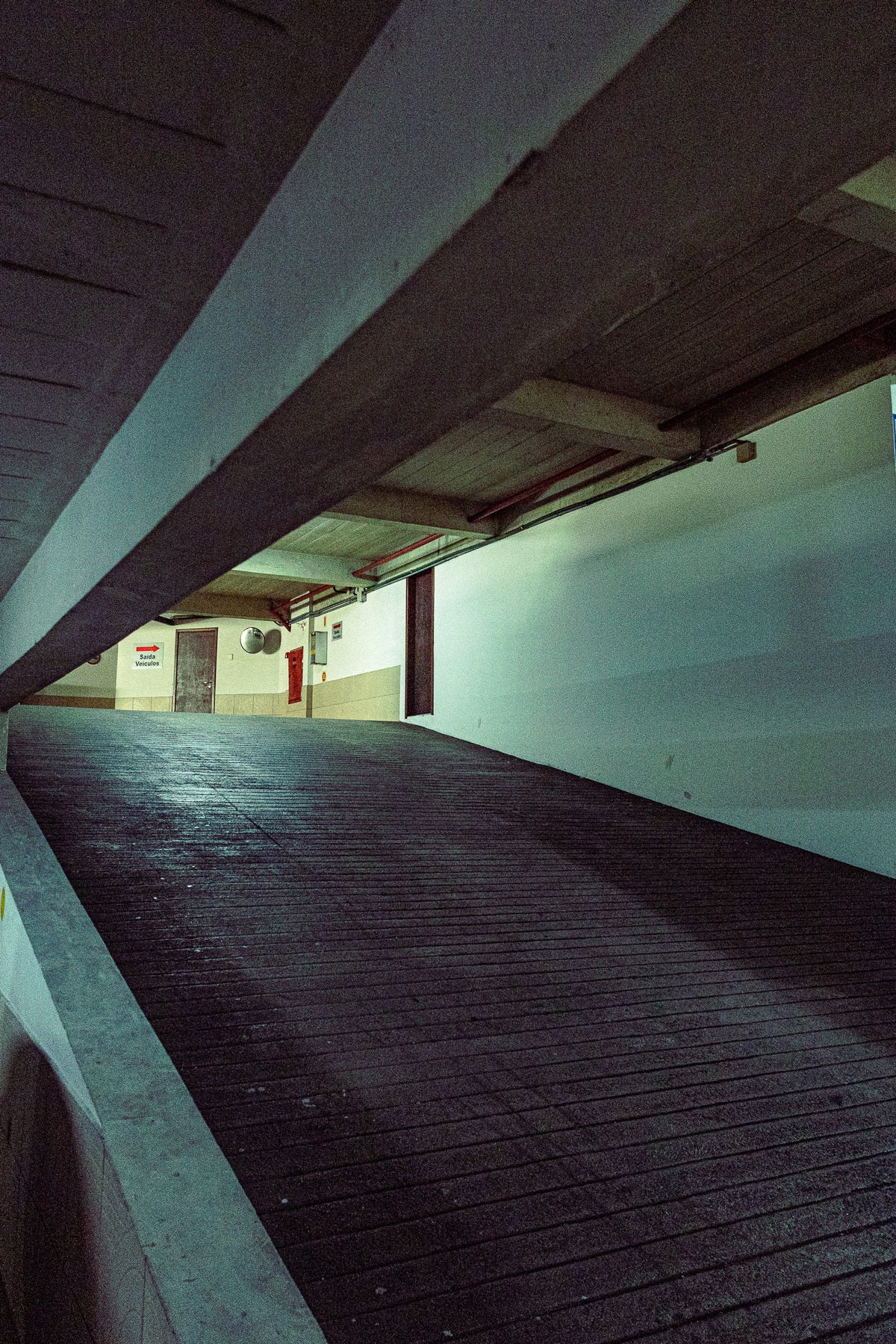 Fotografia em perspectiva de um estacionamento no segundo andar de um prédio. A imagem retrata o concreto, valorizando a iluminação, linhas e sombras.