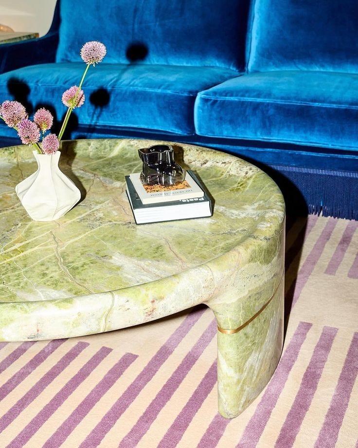 This may contain: a coffee table with flowers on it in front of a blue couch and striped rug
