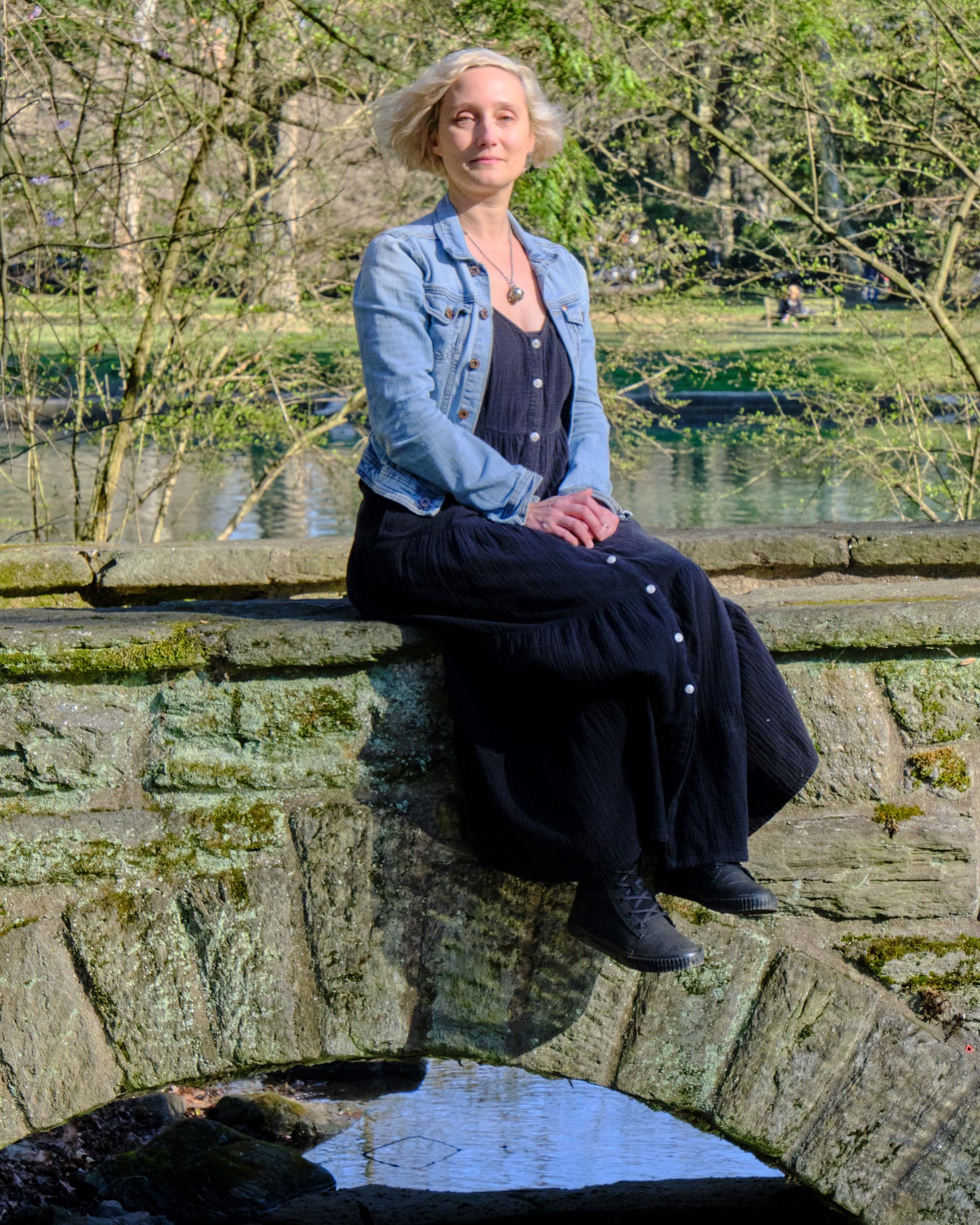 white woman with blond hair sits on a stone bridge in a park