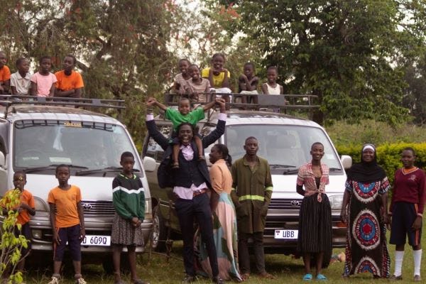 a couple dozen children and adults posed in front of two new white Toyota vans