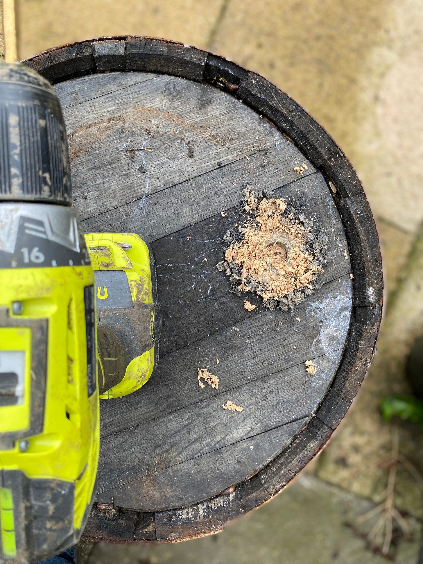 A drill sat upon an upturned wooden barrel, where a drainage hole is being drilled. A drill sat upon an upturned wooden barrel, where a drainage hole is being drilled.