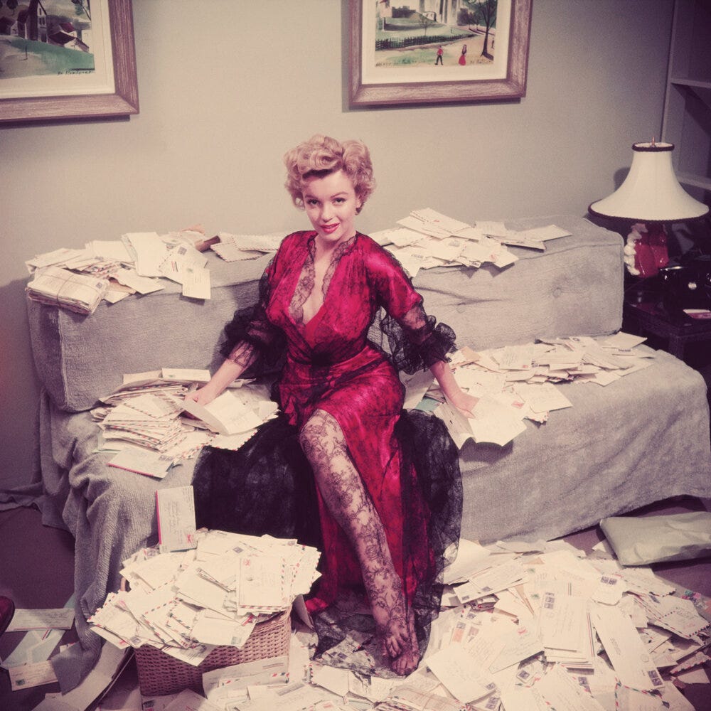 A photo of Marilyn Monroe posing on a couch with letters all strewn about. She's wearing a lacy silk dress/robe.