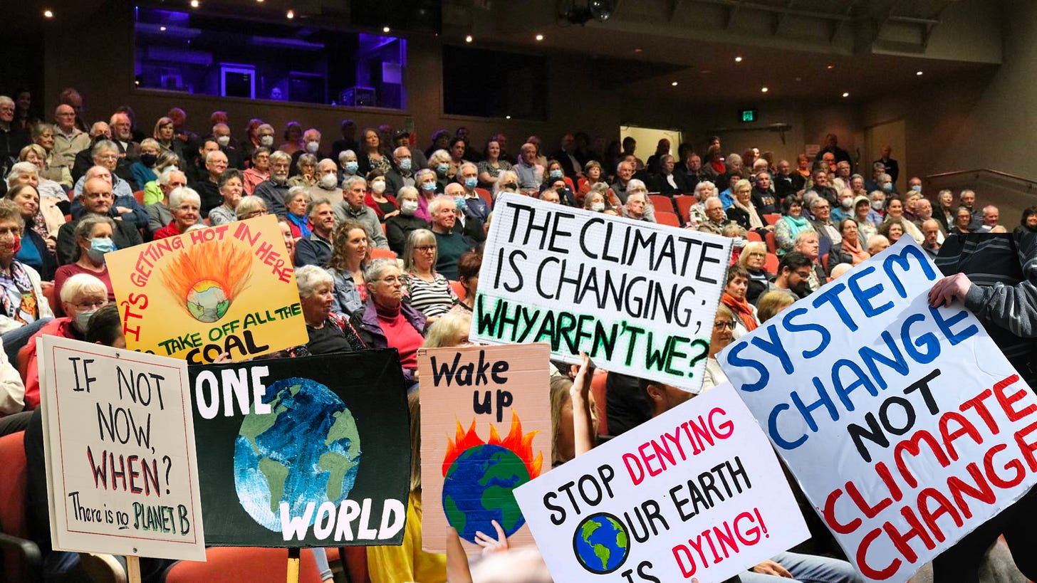 An auditorium of mostly senior, Pākeha folks. Photoshopped on top are climate signs with slogans like "The climate is changing, why aren't we?" and "System change not climate change."