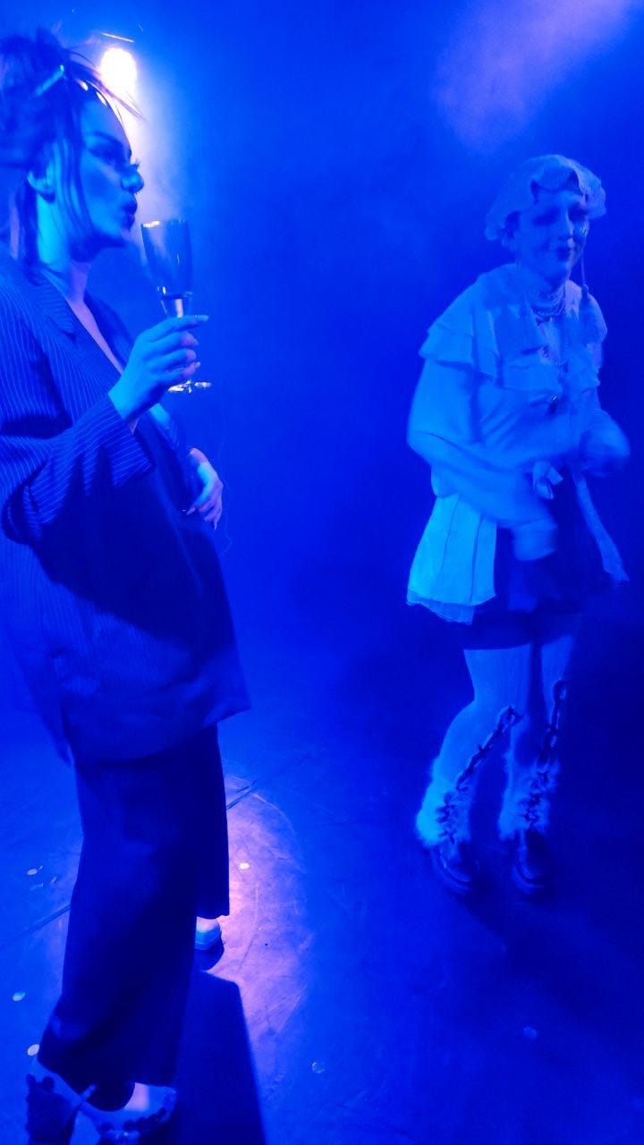 Foto in blauem Licht, links ich mit Anzug und Drag-Makeup und Sektglas, rechts Tobi Honest in weißem Kostüm mit Häkeldecke als Mütze und Drag Makeup Foto in blauem Licht, links ich mit Anzug und Drag-Makeup und Sektglas, rechts Tobi Honest in weißem Kostüm mit Häkeldecke als Mütze und Drag Makeup