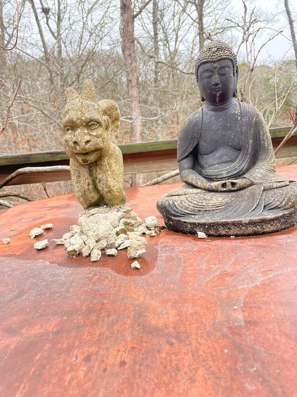 photgraph of two small statues on a plywood table. One is a sitting Buddha, the other is a miniature garygole of the type seen on some medieval cathedrals. The gargoyle is made of cement and its base is crumbling..