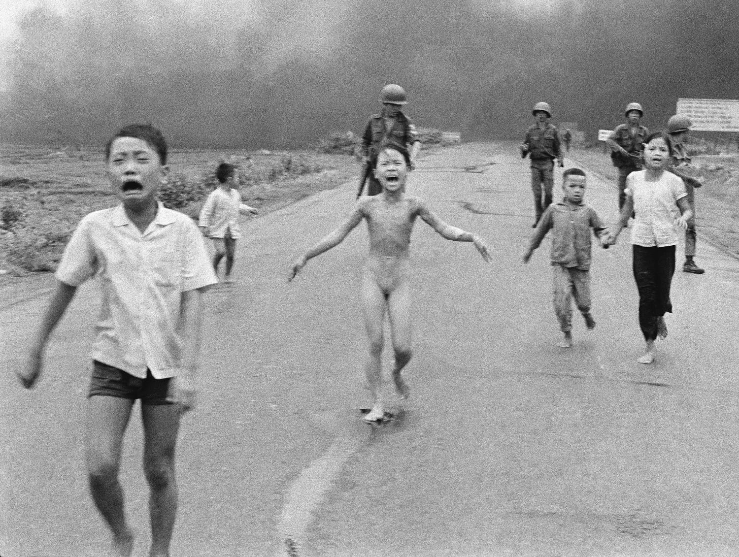 Black and white photo of children running on a road, with a naked girl in the center screaming in pain, and soldiers in the background.