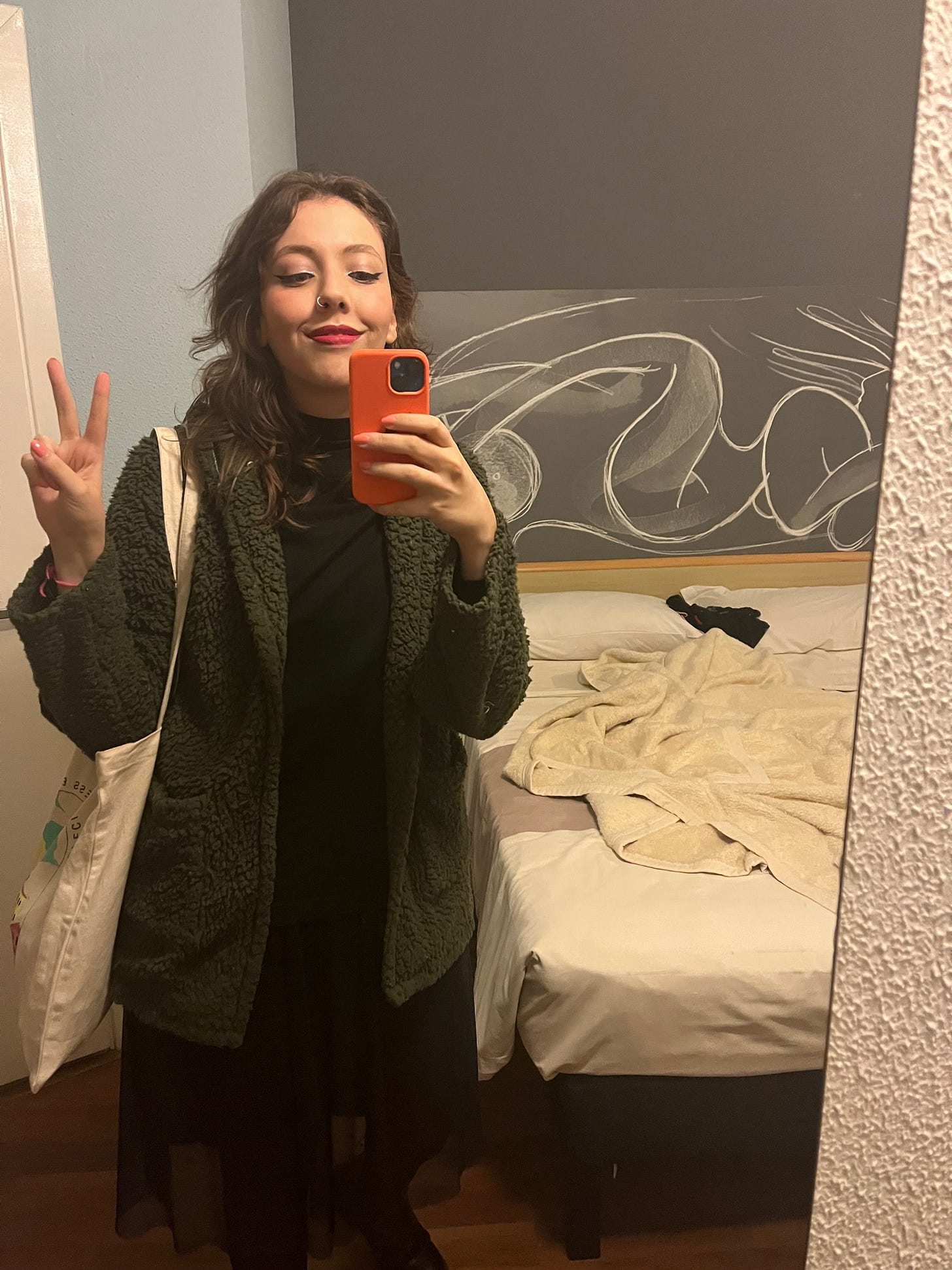 Selfie de look tirada no espelho do hotel: estou toda de preto, com um casaco verde musgo que parece de pelúcia. Delineador gatinho com glitter nos olhos e batom fúcsia.