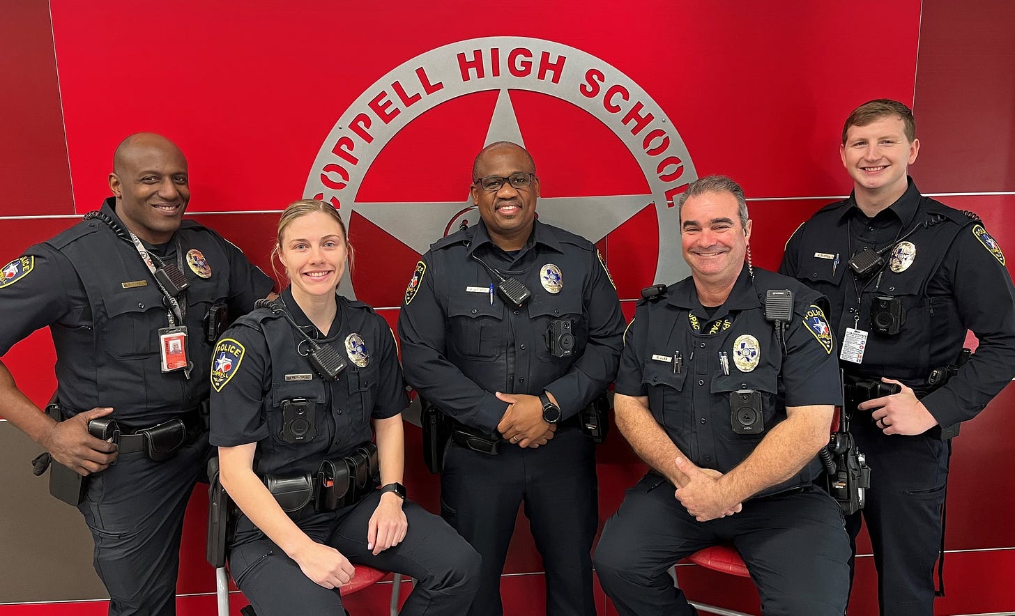 Five smiling police officers in front of a Coppell High School sign