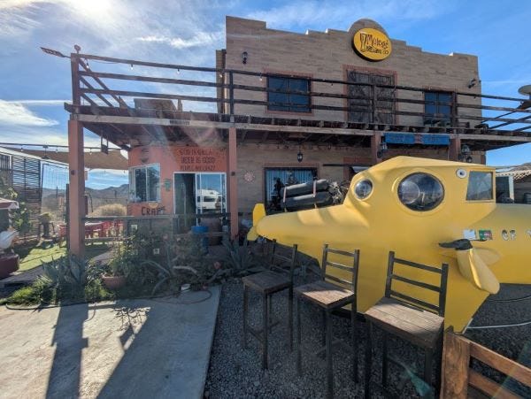 a building labeled Mulege Brewing with a yellow submarine out front. the building is orange terra cotta with a sign that says God is great, beer is good, people are crazy