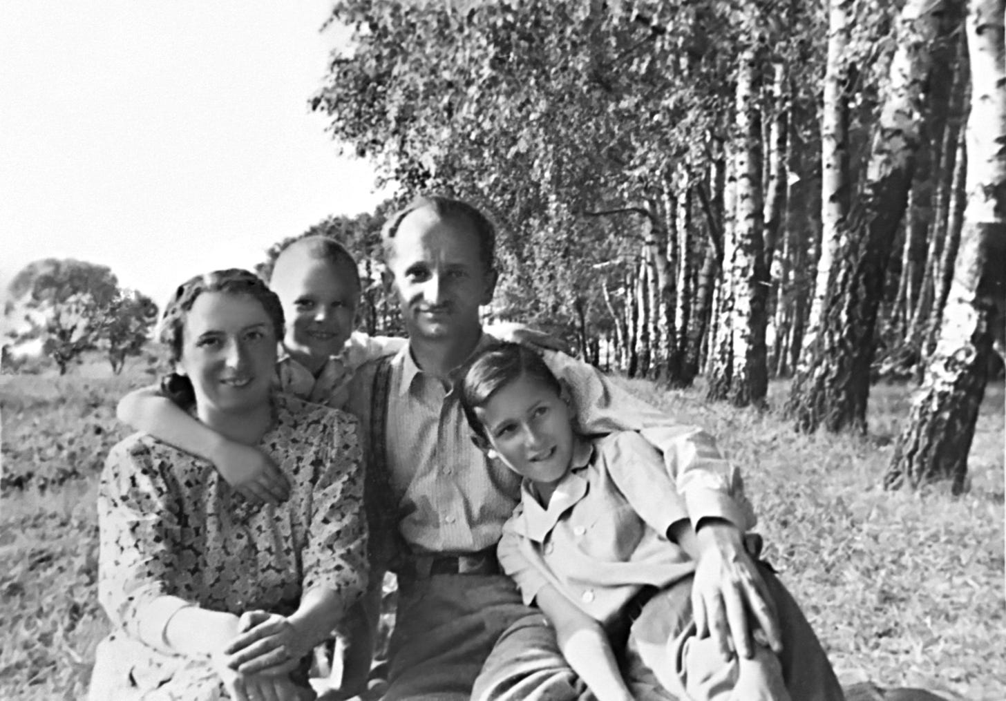 Image description: an outdoor photo of young Michael standing behind his mother and father, with his older brother, Stanisław, seated, with trees in the background.