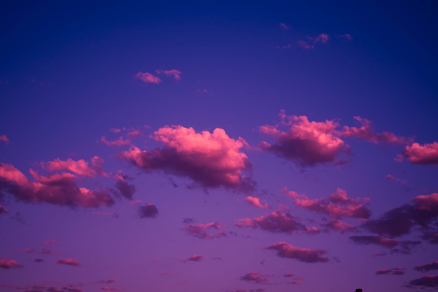 A different vibrant sky shading from blue to violet, crossed by a train of happy little pink clouds.